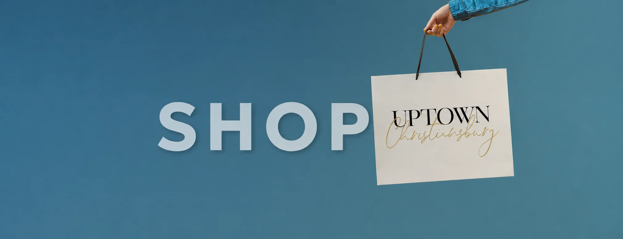 Shop Uptown Christiansburg: a hand holding an Uptown Christiansburg shopping bag